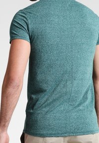Green heathered short-sleeve T-shirt made of soft fabric, featuring a fitted shape and a smooth texture. No visible logos or patterns.
