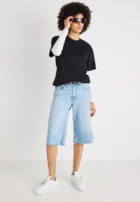 Juodas medvilninis marškinėliai, mėlyni džinsiniai kulotai su nutrintais kraštais, balti ilgomis rankovėmis apykaklės, balti sportbačiai ir tamsūs saulės akiniai.