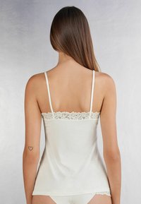 Vit linne med justerbara axelband, spetsdetaljer längs utfskärningen, mjukt tyg och avslappnad passform. Slät textur utan mönster.