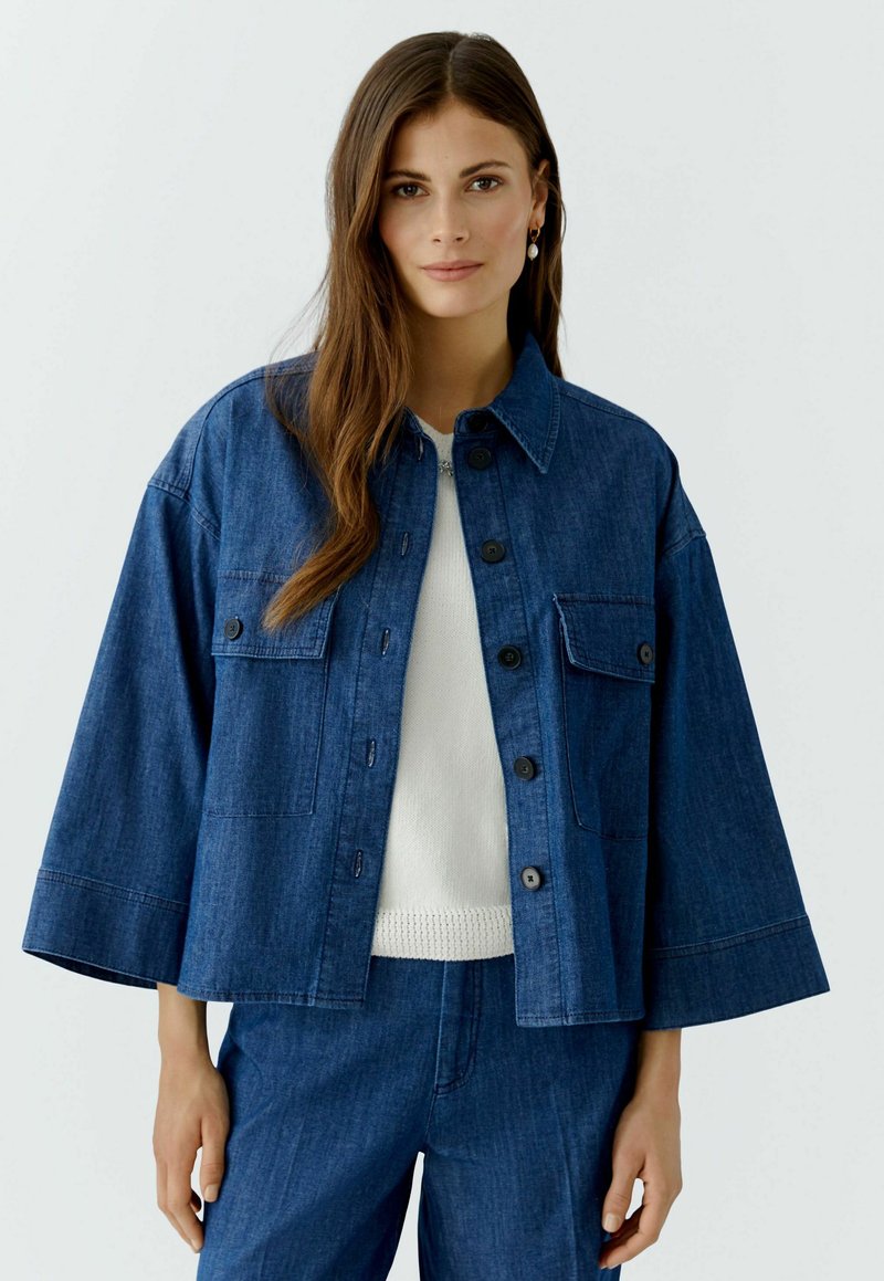 Jeansjack met een recht model, knoopsluiting, borstzak en ruime mouwen. Donkerblauwe kleur en gemêleerde stof. Draag het over een wit topje.