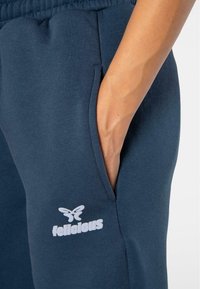 Los pantalones de chándal de algodón en azul marino cuentan con un bolsillo lateral y una marca en blanco. La tela tiene una textura suave y una cinturilla elástica.
