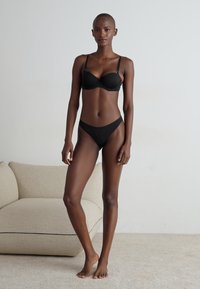Black lingerie set featuring a padded bra with adjustable straps and a matching thong. Smooth fabric with minimalistic design elements.