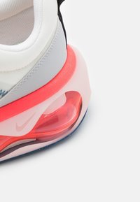 Nike tenisky s bílým a šedým síťovaným svrškem, černými akcenty a viditelnou vzduchovou komorou v jasně růžové barvě na průhledné podrážce. Texturované designové prvky.