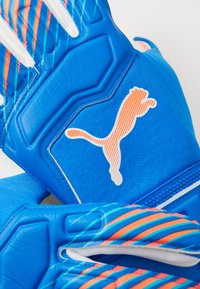 Kék sportkesztyűk strukturált markolattal, narancssárga és fehér díszítéssel, a hangsúlyos fehér Puma logóval és egy elegáns, áramvonalas dizájnnal.