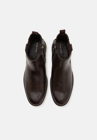 Hnědé kožené kotníkové boty s hladkým povrchem, kulatou špičkou, bočními zipy a poutkem na zadní straně pro snadné oblékání.