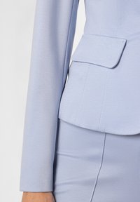 Hellblaues, tailliertes Blazerjackett mit strukturiertem Design, texturiertem Stoff und einer einzelnen Klapptasche auf der Vorderseite, kombiniert mit einem passenden Rock.