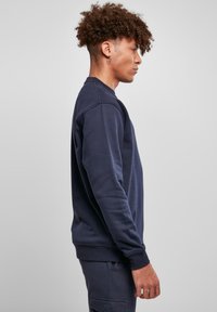 Sudadera de color azul marino oscuro, hecha de tela suave, con un corte regular, puños acanalados y cuello redondo. Sin logotipos ni patrones visibles.