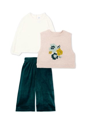 Chemise blanche à manches longues, gilet en tricot sans manches beige avec un motif de fleurs bleues et jaunes, et pantalon large en velours vert foncé.