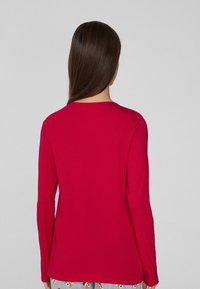 T-shirt à manches longues, col rond en rouge vif, fabriqué en mélange de coton. Texture lisse avec une coupe régulière, mettant en avant un design simple sans accents.