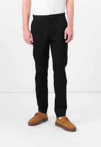 Black trousers made of smooth cotton, featuring a straight fit, front pockets, and a button closure. Paired with brown suede shoes.