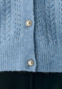 Ljusblå stickad cardigan med ett texturerat mönster, med två pärlliknande knappar och en mjuk, fluffig yta.