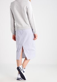 Sudadera gris con puños acanalados, combinada con una falda midi de rayas que presenta una abertura trasera. Complementada con zapatillas blancas con detalles negros.