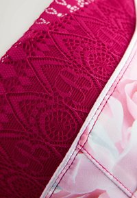 Sutien din dantelă, realizat dintr-un material texturat roz intens, decorat cu un imprimeu floral roz, cu cusături albe pe margini pentru contrast.