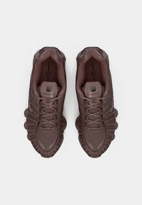 Brown mesh and synthetic athletic shoes with rounded cushioning soles, lacing system, and textured overlays. Nike Shox branding visible.