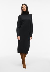 Svart poloklänning med långa ärmar, ribbade muddar och fåll. Kombinerad med knähöga beiga mockastövlar. Enkel och elegant design.