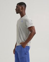 T-shirt in cotone grigio con maniche corte, caratterizzata da testo blu "Lee" e "Crayola". Abbinata a pantaloni in corduroy blu, con tasche laterali visibili.