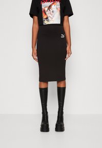 Černé grafické tričko s odvážným potiskem, v kombinaci s přiléhavou černou midi sukni. Model nosí černé lesklé kožené boty po kolena.