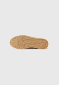 Tan sneaker sole with textured rubber, featuring a diamond pattern and circular accent. Smooth edges and durable material ensure grip.