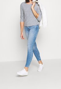 Pasiasty szary długi rękaw, jasnoniebieskie wąskie dżinsy i białe sneakersy. Strój ma swobodny design z czystym wykończeniem i miękką teksturą.