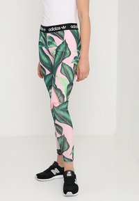 Legíny Adidas s černým páskem, s růžovým pozadím zdobeným velkými zelenými listovými vzory. Ušitý design, vhodné pro aktivní nošení.