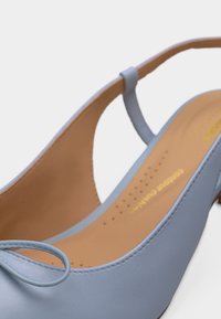 Világoskék slingback magassarkú, lekerekített orral, kis masni részlettel és barna párnázott talpbéléssel, fehér háttéren.