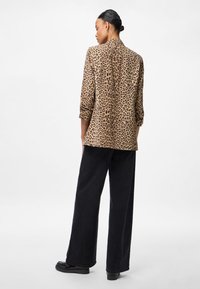 Μπλέιζερ με σχέδιο λεοπάρ σε καφέ και μαύρο, με κομψή γραμμή, τρία τέταρτα μανίκια και άνοιγμα στην πλάτη. Φοριέται με φαρδιά μαύρα παντελόνια και υποδήματα.