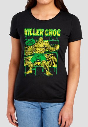 Woman wearing black t-shirt with green and yellow graphic of muscular reptile character labeled "Killer Croc" saying "I am beautiful."