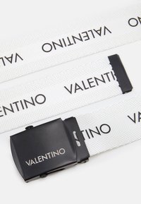 Baltas audinio diržas su pakartotu juodu tekstu "VALENTINO". Yra juodas metalinis užsegimas su lygiu paviršiumi ir funkciškai veikiančiu reguliavimo mechanizmu.