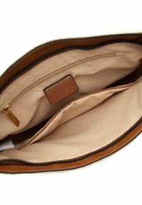 À l'intérieur d'un sac avec des accents en cuir marron, comportant une poche zippée et deux compartiments ouverts, doublé de tissu beige.