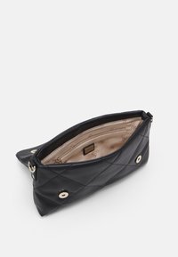 Mustakudottu nahkalaukku terävillä päillä. Kullansävyinen metalliosien ja beigen sisustuksen kanssa varustettu malli, jossa on vetoketjullinen tasku ja logokuosi.