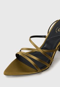 Oliven grøn strappy høyhælte sandal med spiss tå, som har satengoverflate og svart indre fôr. Høyhælte design med åpne sider.