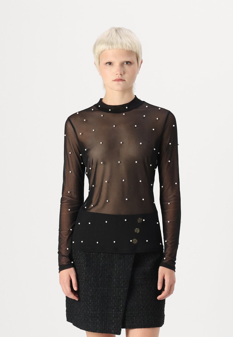 Fekete áttetsző, hosszú ujjú blúz, szétszórt fehér gyöngyökkel és kerek nyakkivágással, hozzá egy textúrált fekete szoknya gombokkal.