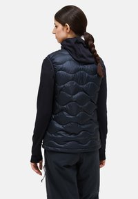 Navy quilted puffer vest with a high collar, featuring a smooth exterior and textured fabric sleeves. Black pants are also visible.