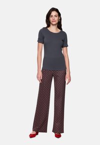 Graumeliertes Kurzarmoberteil kombiniert mit weit geschnittenen, gemusterten Hosen in Dunkelrot mit geometrischem Design. Kombiniert mit roten Schuhen.