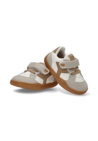 Zapatillas infantiles en blanco y beige, con una correa de velcro, tela texturizada, suela de goma y un diseño geométrico en los laterales.