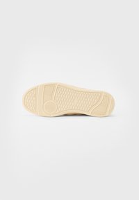 Sneakerska potplate boje kreme s teksturiranim uzorkom za prihvaćanje i kružnim akcentima. Izrađena od gume s glatkom površinom.