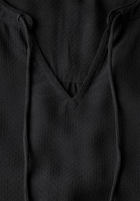 Zwarte, lichtgewicht hoodie met een V-hals en trekkoorden. De stof heeft een gestructureerd patroon met kleine perforaties overal.