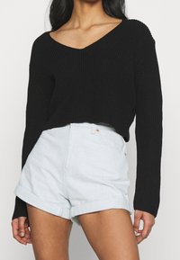 Schwarzer Strickpullover mit tiefem V-Ausschnitt und langen Ärmeln, kombiniert mit hellblauen Jeansshorts mit umgeschlagenem Saum. Glatte Textur und lockere Passform.