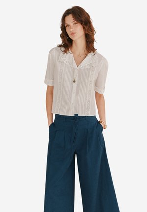 Blusa bianca a maniche corte con pieghe e bordo in pizzo, abbinata a pantaloni blu navy a gamba larga e vita con laccio.