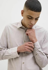Camisa de manga larga gris claro con cuello, textura suave y detalles de botones en los puños. Patrón jaspeado sutil visible.