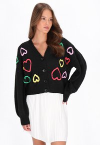 Svart kortärmad cardigan med färgglada stickade hjärtmotiv. Har en djup V-ringning och femknappslåsning. Mjuk textur, långa ärmar.