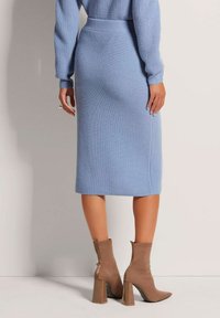 Helles blaues, geripptes Strickrock mit einer taillierten Silhouette, kombiniert mit beigen Knöchelschuhen, die einen auffälligen Absatz und Reißverschlussakzente haben.