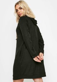 Svart ribbad hoodie klänning med huva, långa ärmar, sidfickor och en detalj med paljetter på ryggen.