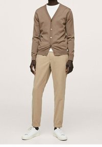 Brown knitted cardigan with a v-neck and button closure. Paired with beige tapered pants and white sneakers. Smooth texture, casual design.