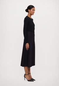 Musta pitkähihainen paita yhdistettynä tummaan, valuvaan hameeseen. Mallilla on päällään piikkikorkoiset mustat kengät, jotka korostavat sulavaa, hoikkaa siluettia.