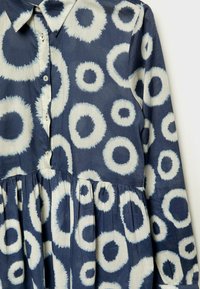 Robe bleu marine à manches longues avec motifs circulaires blancs irréguliers, boutonnée sur le devant, col et détail froncé à la taille.