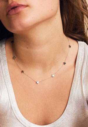 Silver star necklace with a delicate chain featuring multiple star-shaped accents, set against a light, textured top.