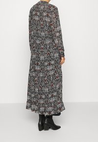 Pitkähihaisen mustan kukkamekon, jossa on kuvioitu muotoilu punaisilla ja valkoisilla yksityiskohdilla, röyhelöhelma ja joka on yhdistetty mustiin korkokenkiin.