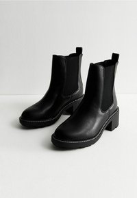 Czarne skórzane botki za kostkę z elastycznymi panelami bocznymi, kwadratowym noskiem i blokowym obcasem. Posiadają białe szwy wzdłuż podeszwy i pętle do zakupu.
