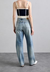 Vaqueros de mezclilla de pierna ancha en azul claro con un acabado desgastado, combinados con un top corto en color marino que presenta tirantes crema y una cinturilla ajustada.